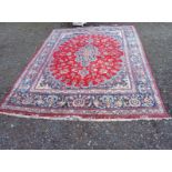 A PERSIAN MESHED RUG OF CARPET PROPORTIONS Having an oval form design on red ground with a wide