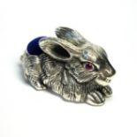 A SILVER NOVELTY RABBIT FORM PIN CUSHION Recumbent pose with blue velvet cushion and paste set eyes.