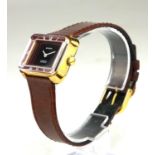 GRUEN, A YELLOW METAL WRISTWATCH Red dial, rectangular case, on brown leather strap. (diameter 29mm)