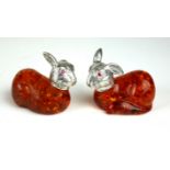 A PAIR OF SILVER AND AMBER FIGURES OF HARES With ruby red glass eyes. (5cm)