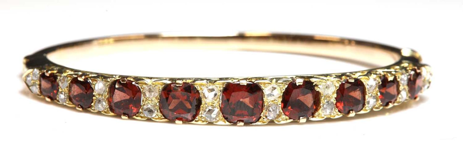 A gold garnet and diamond carved head-style hinged bangle,