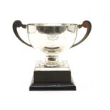 A George V silver twin handled trophy with scroll handles and square plinth base,