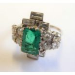 A platinum and diamond dress ring; vertically set with a vertical emerald surmounted with three