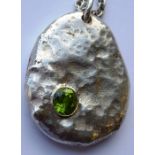 A heavy modern design oval mottled silver pendant of pebble form and set with a hand-cut green
