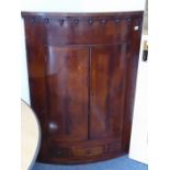 A late 18th century bow-fronted mahogany hanging corner cupboard of large proportions; the cornice
