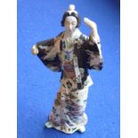 An early 20th century Japanese pottery model of a Geisha; she wears a black jacket decorated with