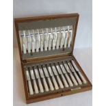 An early 20th century oak-cased set of 12 mother-of-pearl-handled and silver-plate-bladed tea knives