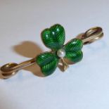 A small yellow metal bar brooch centrally decorated with a green enamel shamrock centred with a