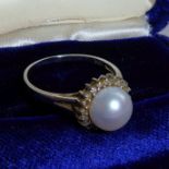 A white metal dress ring marked 14K, centrally set with a pearl surrounded by small hand-cut white