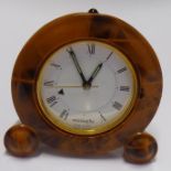 A small travelling alarm clock by Missiaglia; the faux tortoiseshell enamel case surrounding a white
