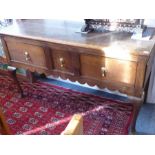 An 18th century oak dresser base; planked top above three frieze drawers, shaped frieze and raised