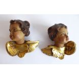 An interesting opposing pair of carved wood cherub heads; naturalistically painted and with gilded