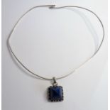 A silver- mounted pendant set with a pyramid-shaped lapis lazuli and suspended from a silver