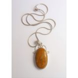 A silver-mounted oval pendant set with a cabochon hardstone in a mottled mustard colour, suspended