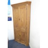 A freestanding pine corner cupboard; the outset cornice above four panelled doors enclosing shelves,