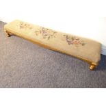 A long footstool having floral needlework tapestry top and gilt-style base on bun feet (127cm wide)