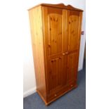 A modern pine wardrobe of slim proportions, two fielded panel doors enclosing hanging space and