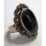 A silver ring centrally set with a vertical oval cabochon black hardstone within a marcasite-mounted