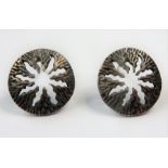 A pair of circular silver earrings having a sunburst effect