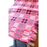 A hand-made Welsh blanket decorated with various stylised geometric shapes etc. against a pink
