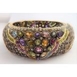 A large bangle profusely set with many diamonds and various other precious stones, marked 18K (total