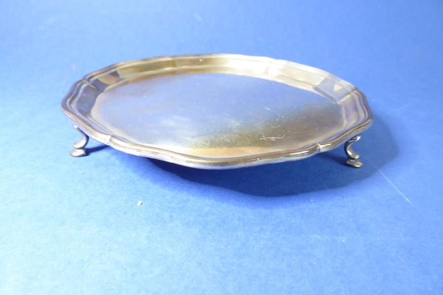 A small hallmarked silver salver with pie-crust edge and raised on three cast feet; Sheffield