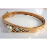 A 19th century rose-gold coloured bangle, centrally set with a pearl flanked each side by three