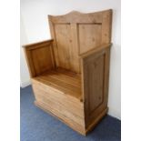 A pine settle; two panelled back above high arms and a hinged storage seat, raised on plinth base