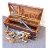 An old stained pine two-handled tool chest containing a variety of tools etc. to include a wooden