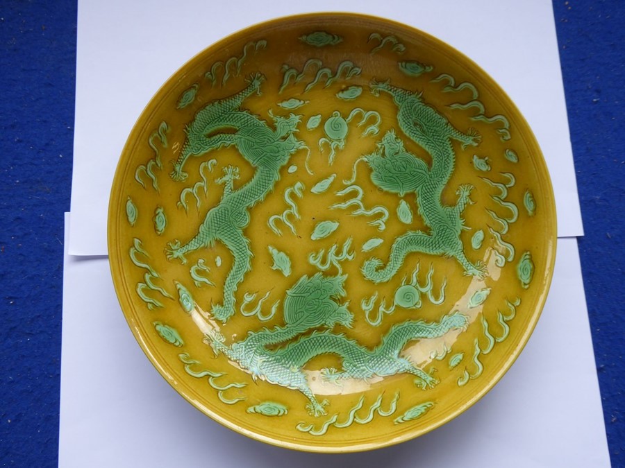 A Chinese porcelain scrafitto dish; three green dragons chasing pearls amongst clouds against an