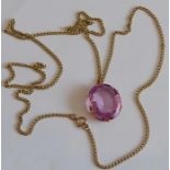 A large hand-cut oval faceted pink topaz set into a yellow-metal mount as a pendant, suspended on