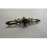 A gold fancy ornate scroll bar brooch horizontally set with an oval faceted possibly spessartite