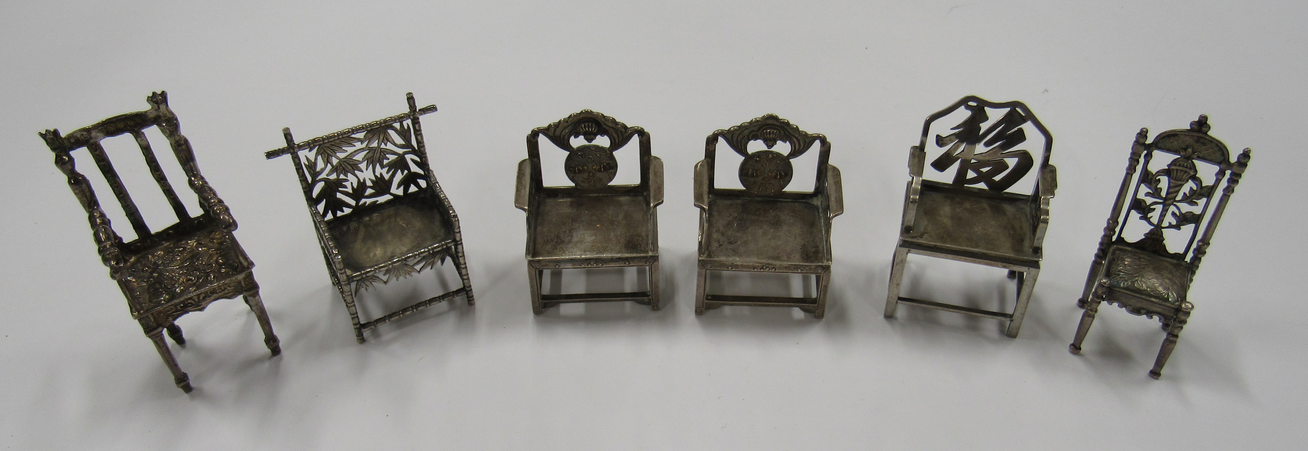 A collection of six silver miniature dolls house chairs, unmatched but with semi backs,