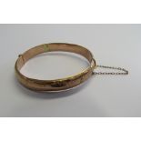 An Edwardian rose gold bangle with half patterned foliate scroll and blank cartouche. Hallmarked