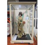 A Japanese doll in traditional Kimono dress holding a musical drum type instrument and stick