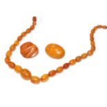 An amber type necklace, length 64cm; and two amber brooches. Necklace - 39.6 grams. Two brooches -