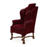 A 17th Century Style Wing-Back Chair, covered in worn red velvet, with rounded arm supports and