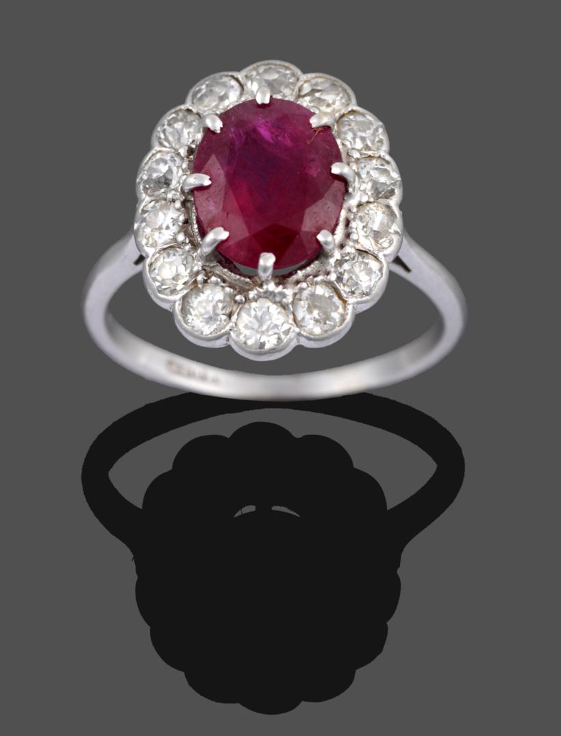 A Ruby and Diamond Cluster Ring, the oval cut ruby in a white claw setting within a border of old