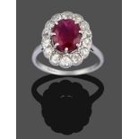 A Ruby and Diamond Cluster Ring, the oval cut ruby in a white claw setting within a border of old