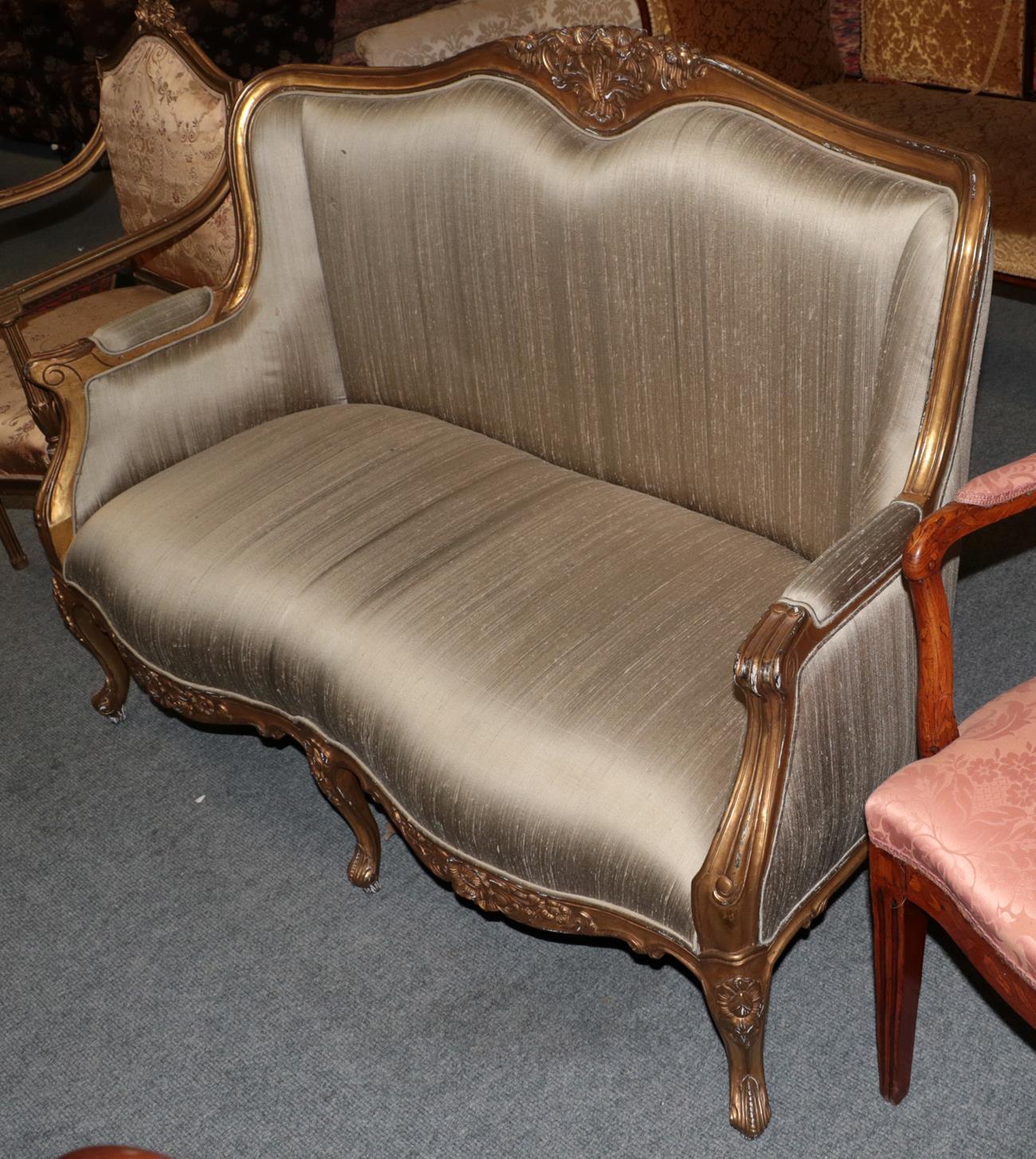 A French gilt framed sofa with floral carved crest and scroll carved down swept arms raised on