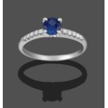 A 14 Carat White Gold Sapphire and Diamond Ring, the round cut sapphire in a four claw setting, to
