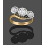 A Diamond Three Stone Twist Ring, the old cut diamonds in white millegrain settings, on a yellow