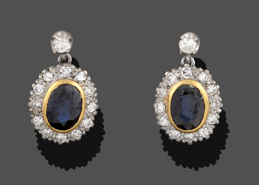 A Pair of Sapphire and Diamond Drop Earrings, the oval cut sapphire in a yellow rubbed over setting,