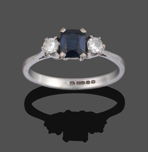 An 18 Carat White Gold Sapphire and Diamond Three Stone Ring, the emerald-cut sapphire sits