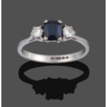 An 18 Carat White Gold Sapphire and Diamond Three Stone Ring, the emerald-cut sapphire sits