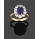A Sapphire and Diamond Cluster Ring, the oval cut sapphire in a yellow claw setting, within a border