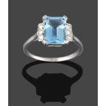 An Aquamarine and Diamond Ring, the emerald-cut aquamarine in white claw settings, flanked by