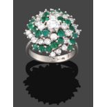 An Emerald and Diamond Cluster Ring, a round brilliant cut diamond within a swirling border of