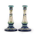 A Pair of Burmantofts Faience Pottery Candlesticks, decorated with flower heads in blues and greens,