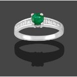 An Emerald and Diamond Ring, the round cut emerald in a white claw setting to baguette cut diamond